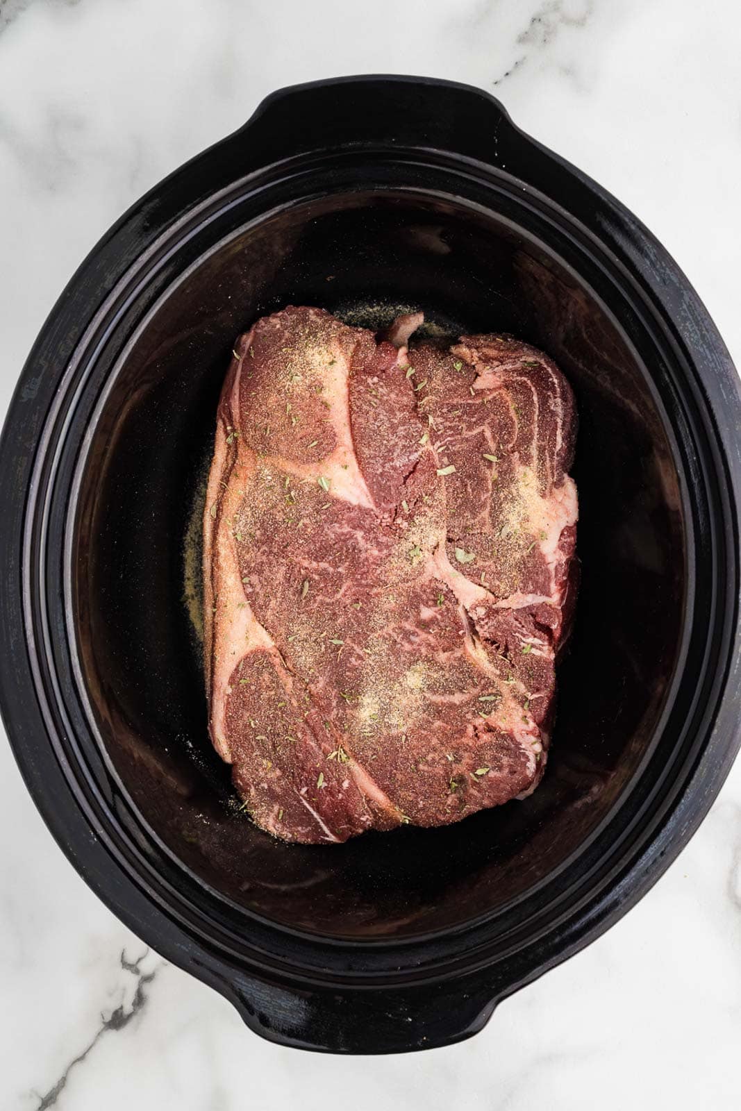 overhead view of seasoned roast in black slow cooker