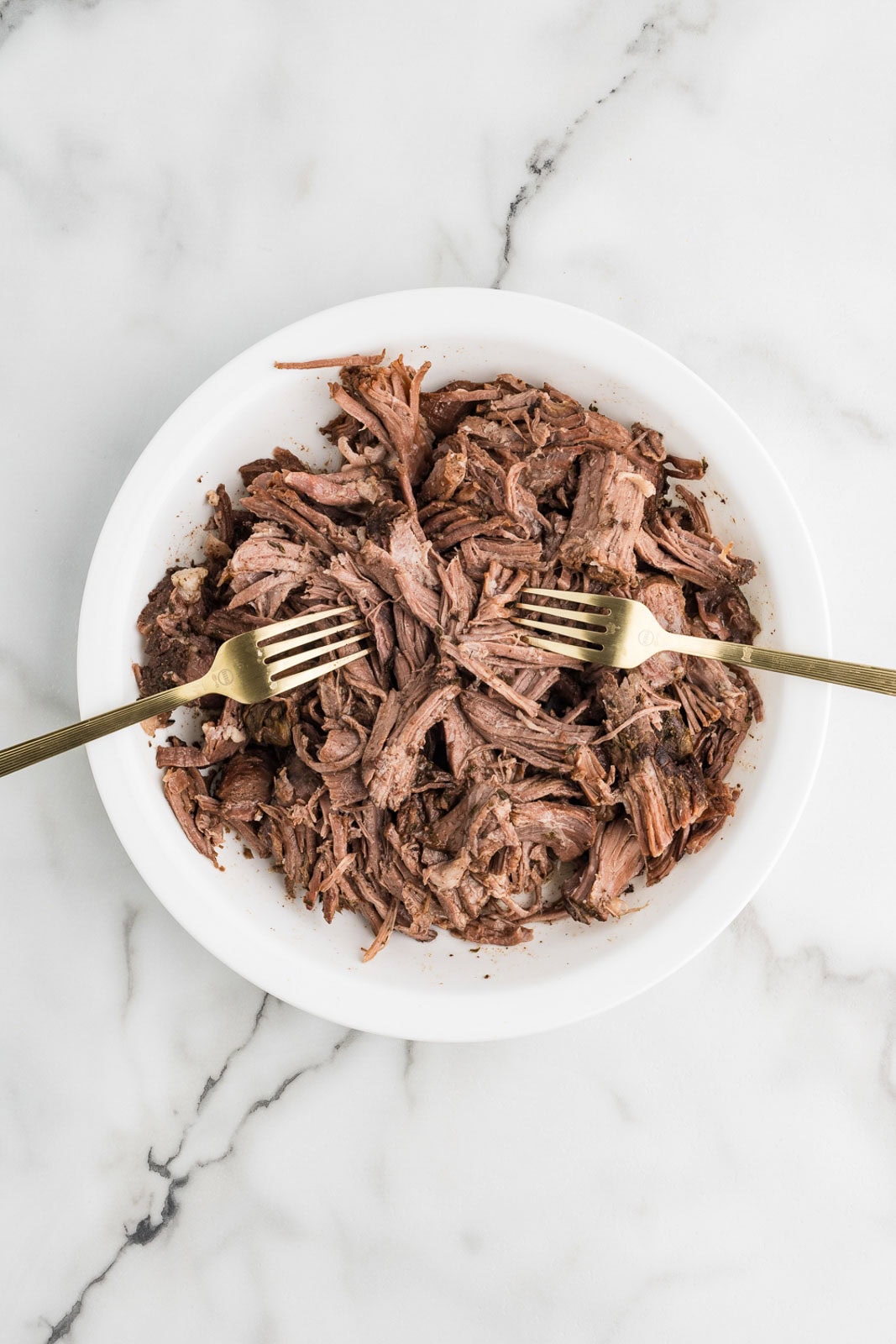 white bowl of shredded roast with 2 forks