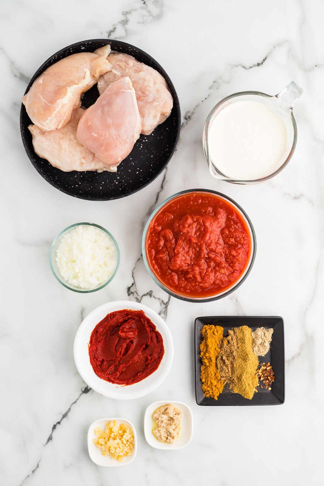 ingredients to include containers of chicken breasts, crushed tomatoes, diced onions, tomato paste, minced garlic, minced ginger, turmeric, garam masala, cumin, cardamom, red pepper flakes, and heavy cream