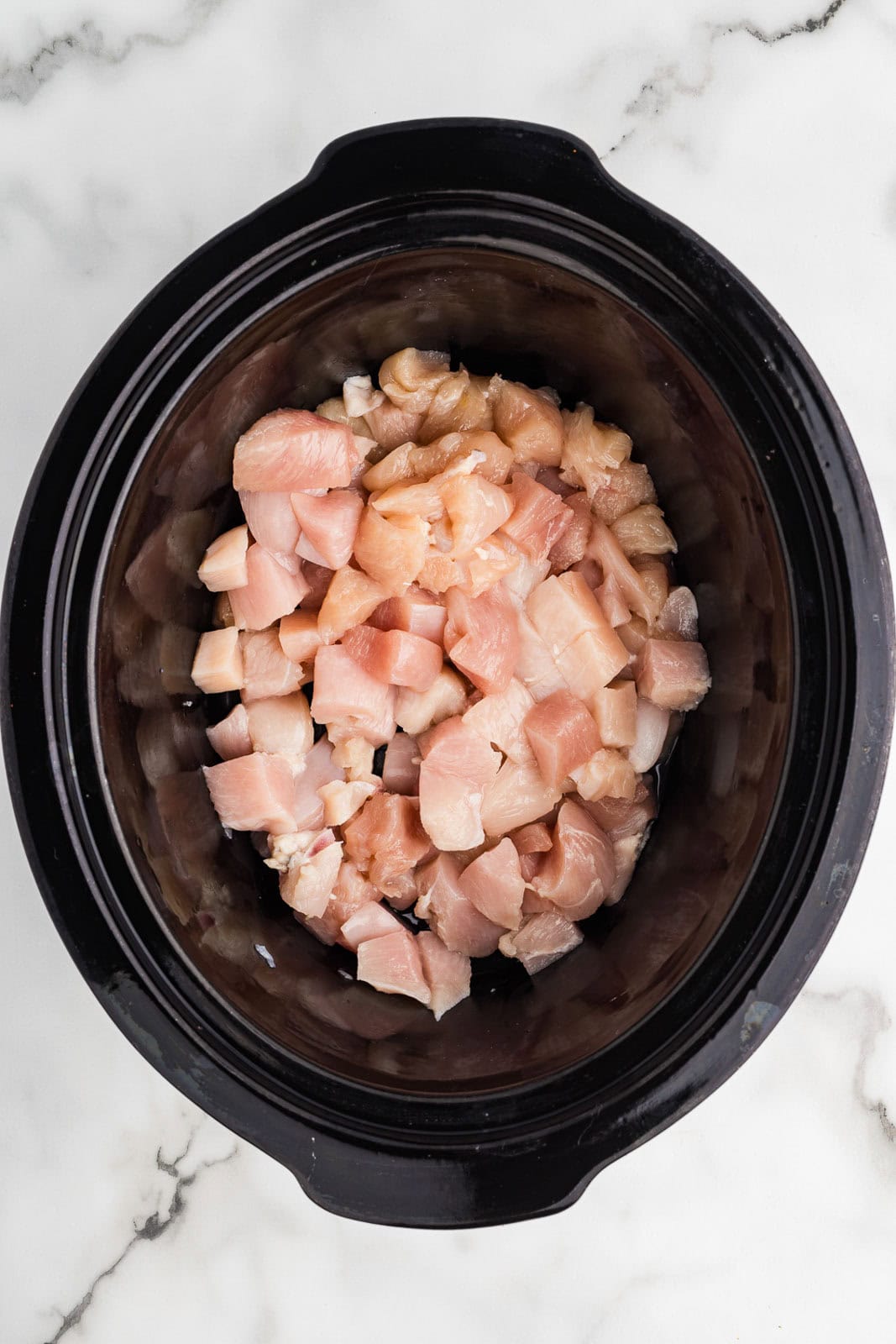 overhead view of black slow cooker with cubed chicken breasts