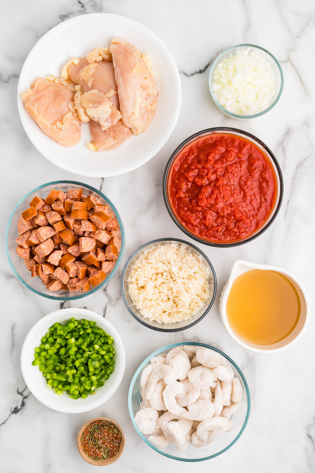 bowls of ingredients to include chicken breasts, diced Andouille sausage, diced green peppers, diced white onion, Creole seasoning, cooked white rice, chicken broth, crushed tomatoes and raw shrimp