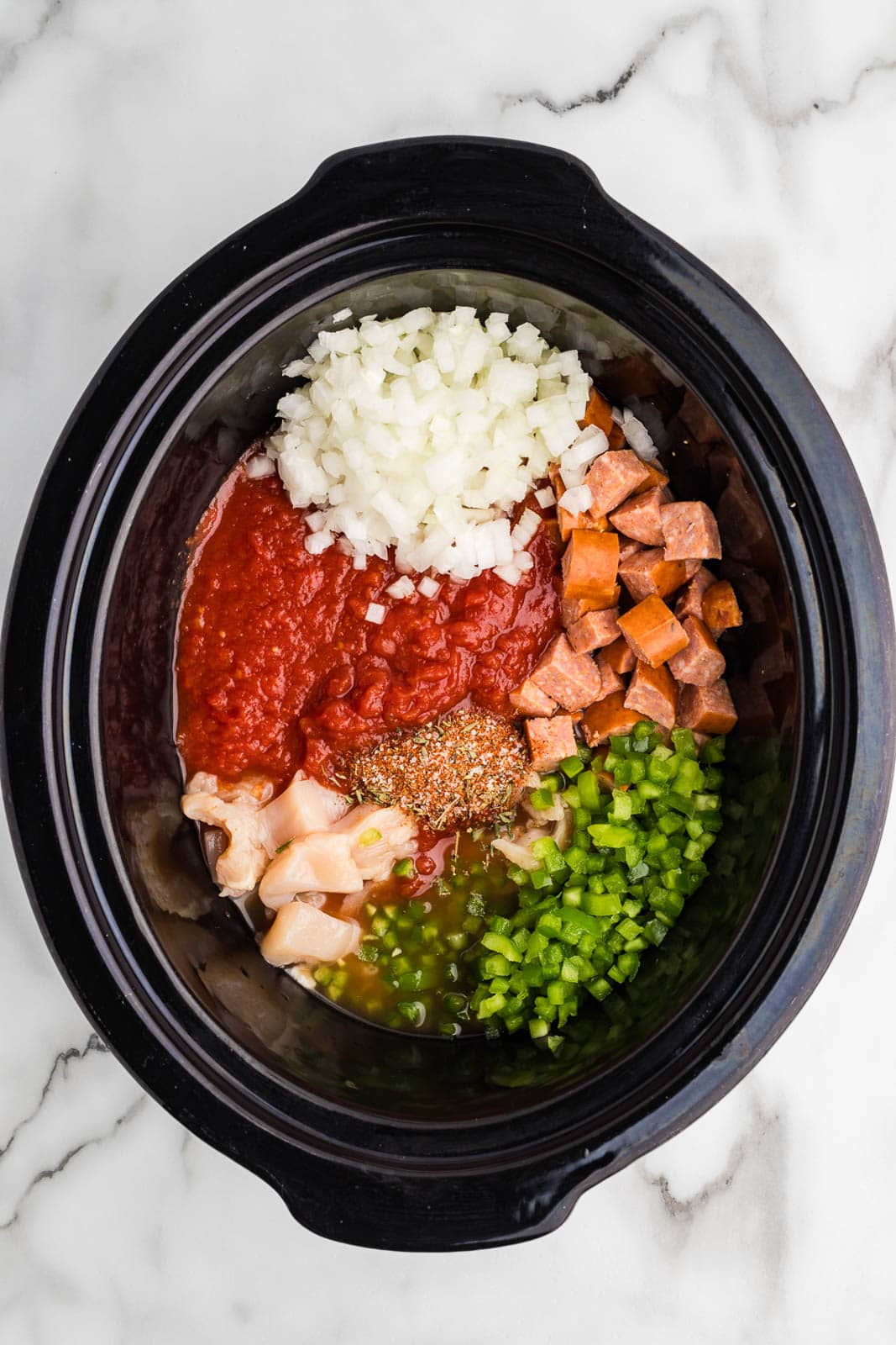black slow cooker with all ingredients added except for shrimp and rice