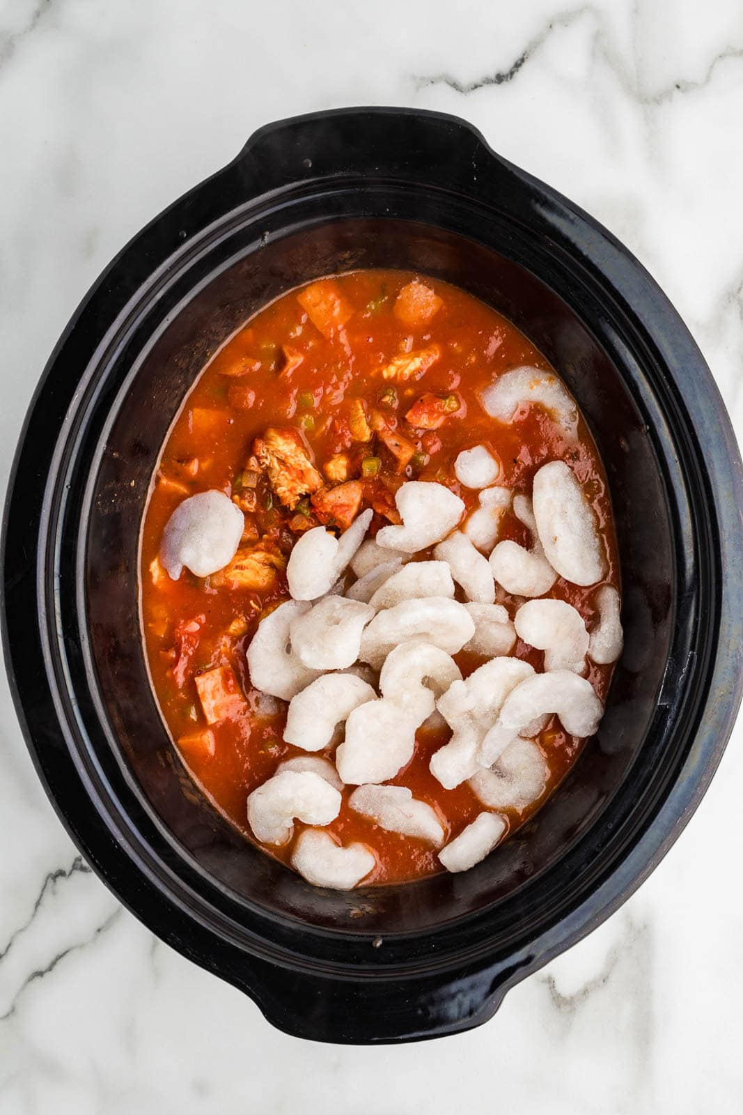 black slow cooker of cooked mixture with raw shrimp added on top