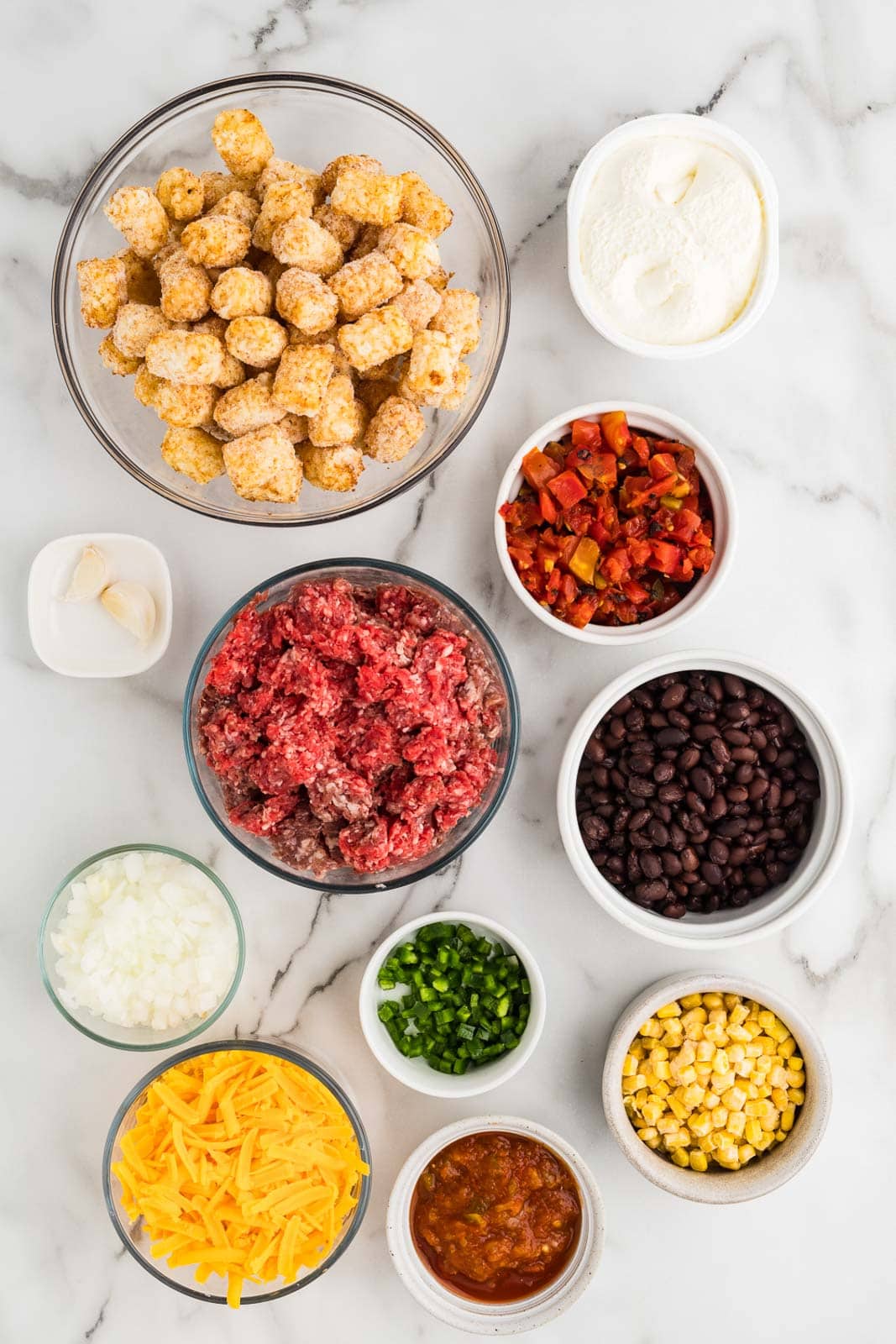 ingredients to include containers of ground beef, diced yellow onion, garlic, diced jalapeno pepper, black beans, fire roasted tomatoes, frozen corn, whipped cream cheese, tater tots, salsa and cheddar cheese