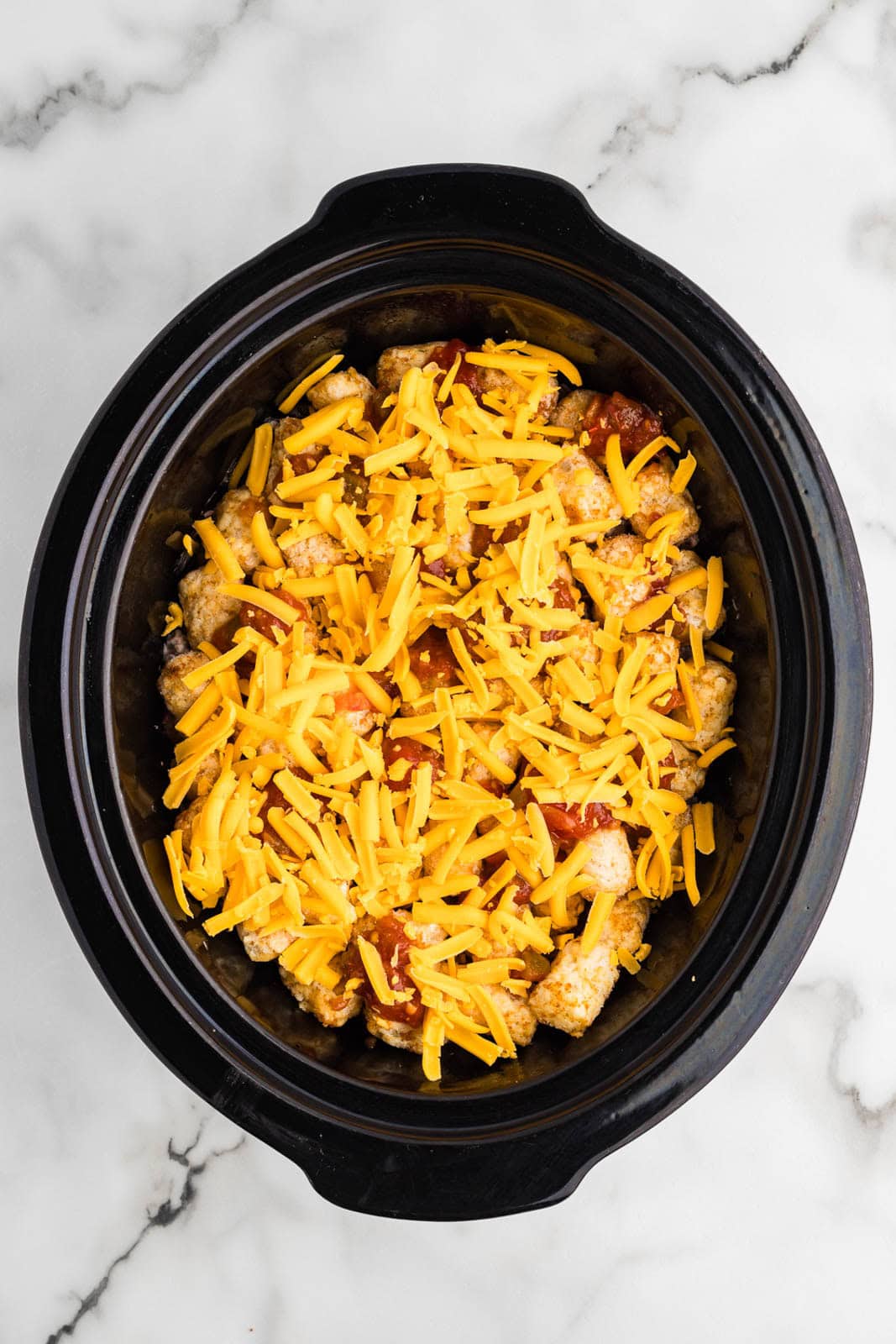 black slow cooker with tater and ground beef mixture, salsa and topped with cheese