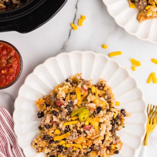 two white dinner plates of tater tot casserole, forks, salsa and black slow cooker in background