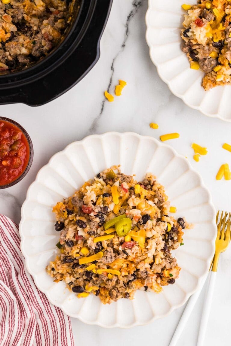 two white dinner plates of tater tot casserole, forks, salsa and black slow cooker in background