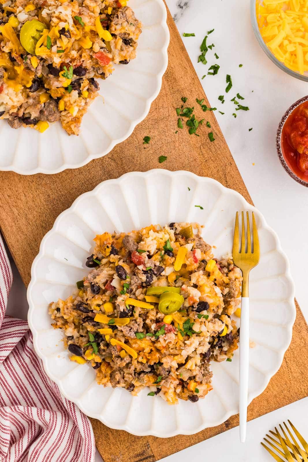 two white dinner plates of tater tot casserole, forks, salsa and cheese