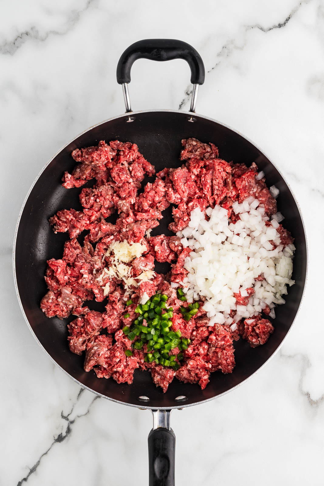 black skillet with ground beef, onions, garlic and jalapeno