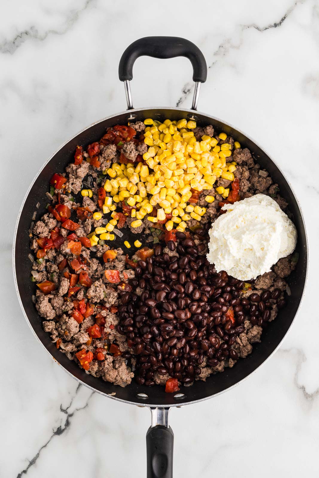 black skillet with ground beef mixture with black beans, tomatoes, corn and cream cheese