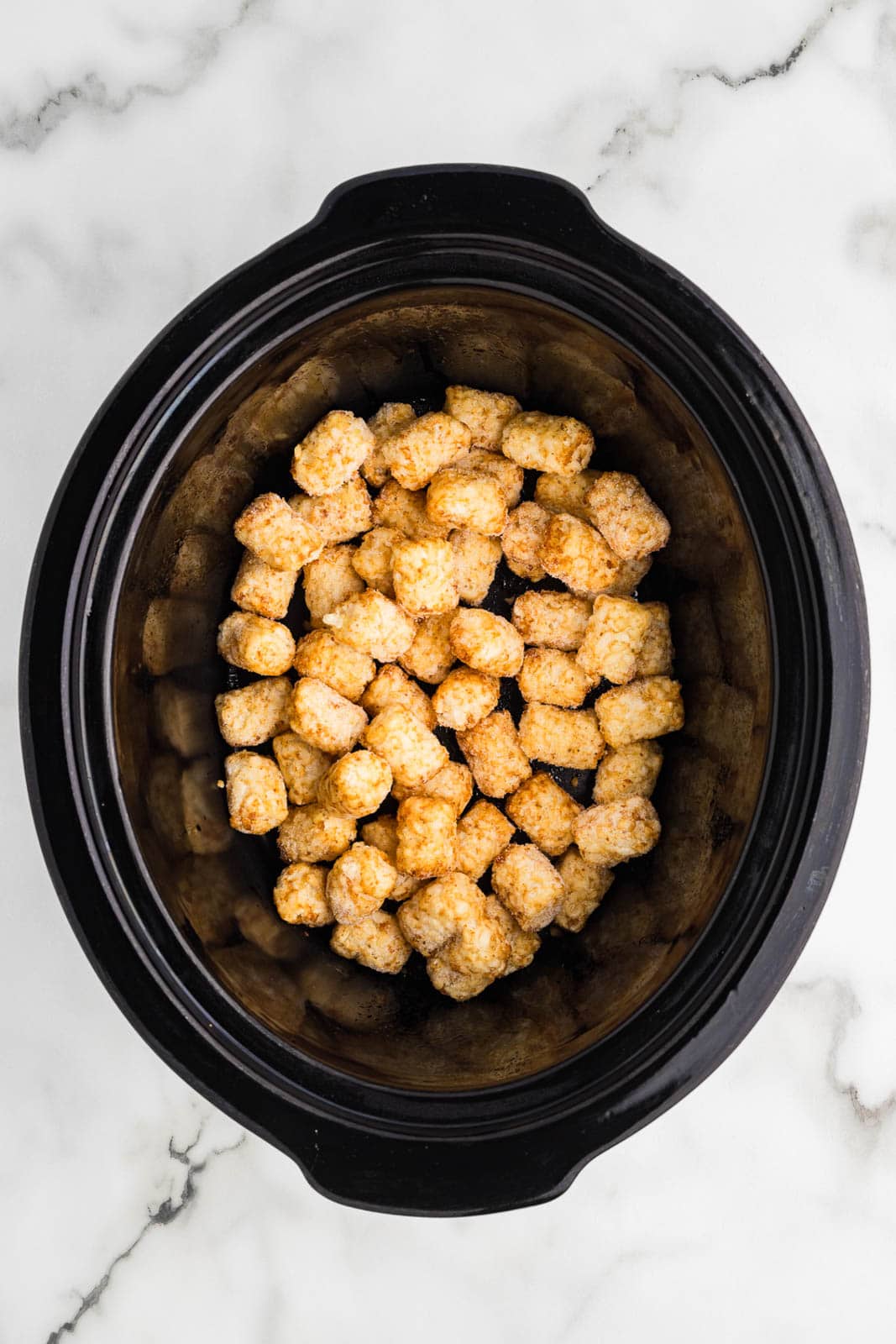 black slow cooker with tater tots on bottom