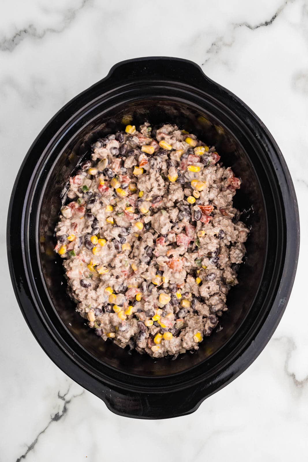 black slow cooker with tater tots and then ground beef mixture on top