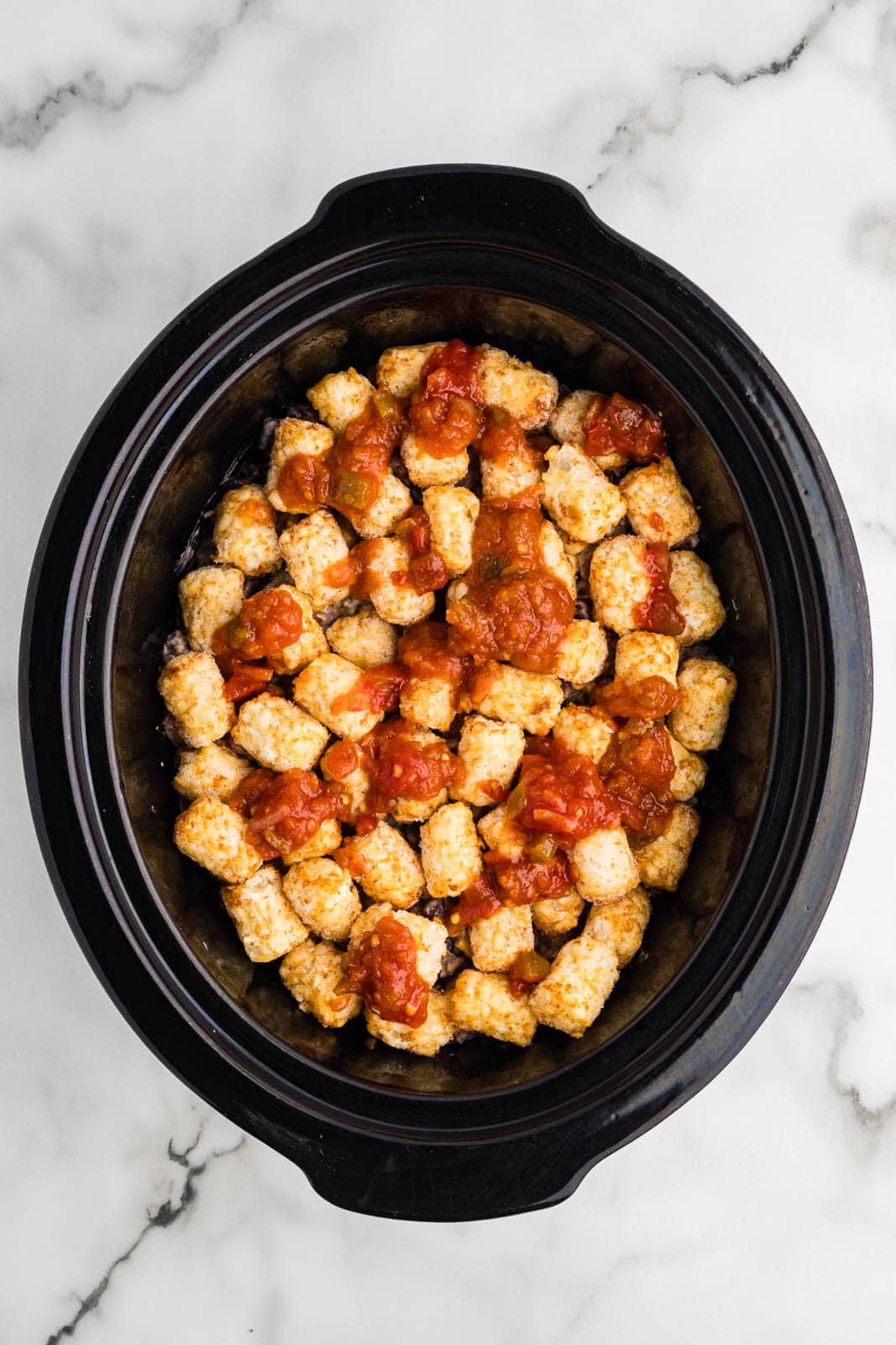 black slow cooker with tater and ground beef mixture topped with salsa