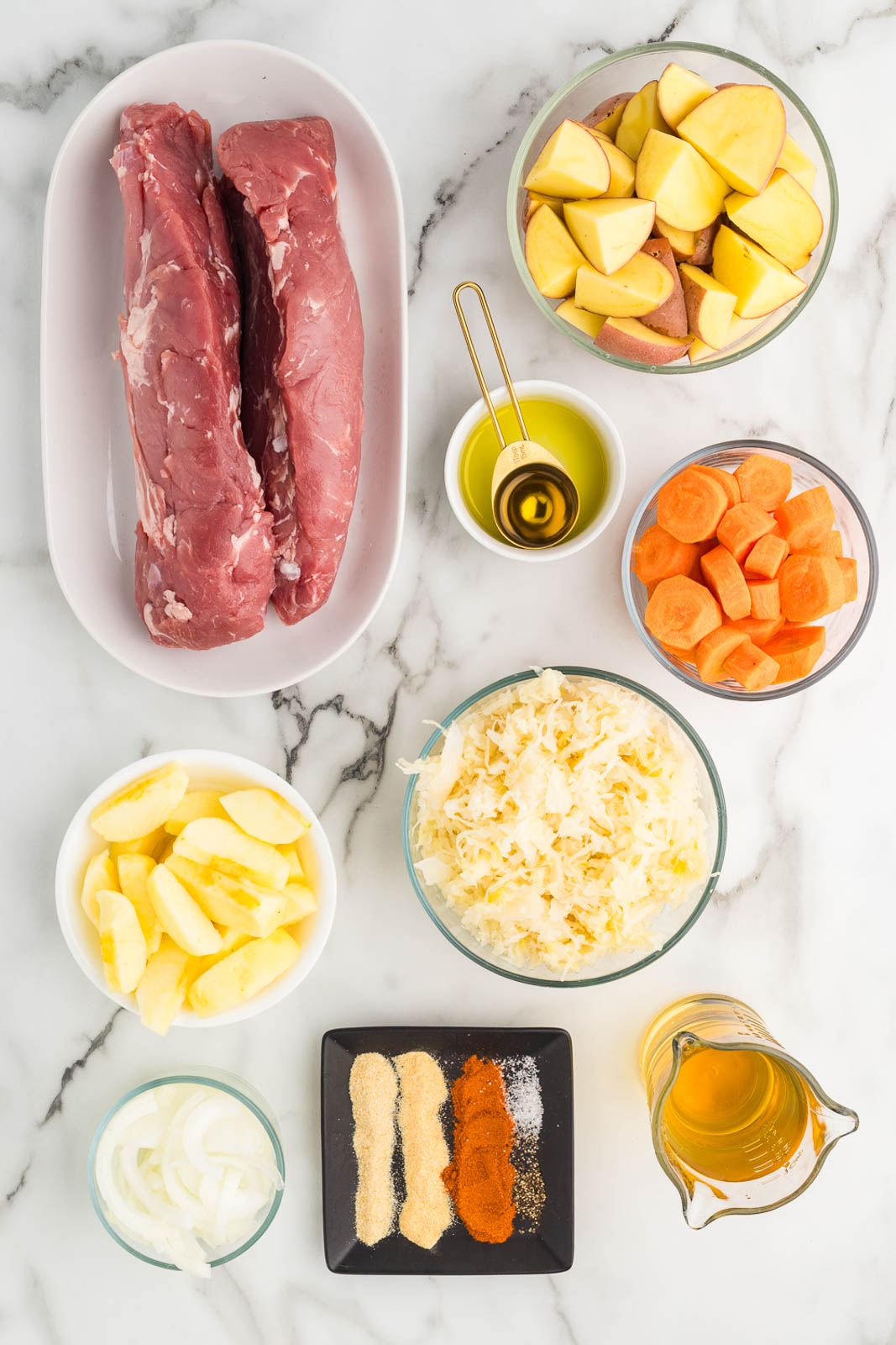 ingredients in containers to include two pieces of pork loin, red potato wedges, sliced carrots, olive oil, sauerkraut, apple slices, apple juice, sliced onion and dry ingredients to include garlic and onion powder, salt, pepper and paprika