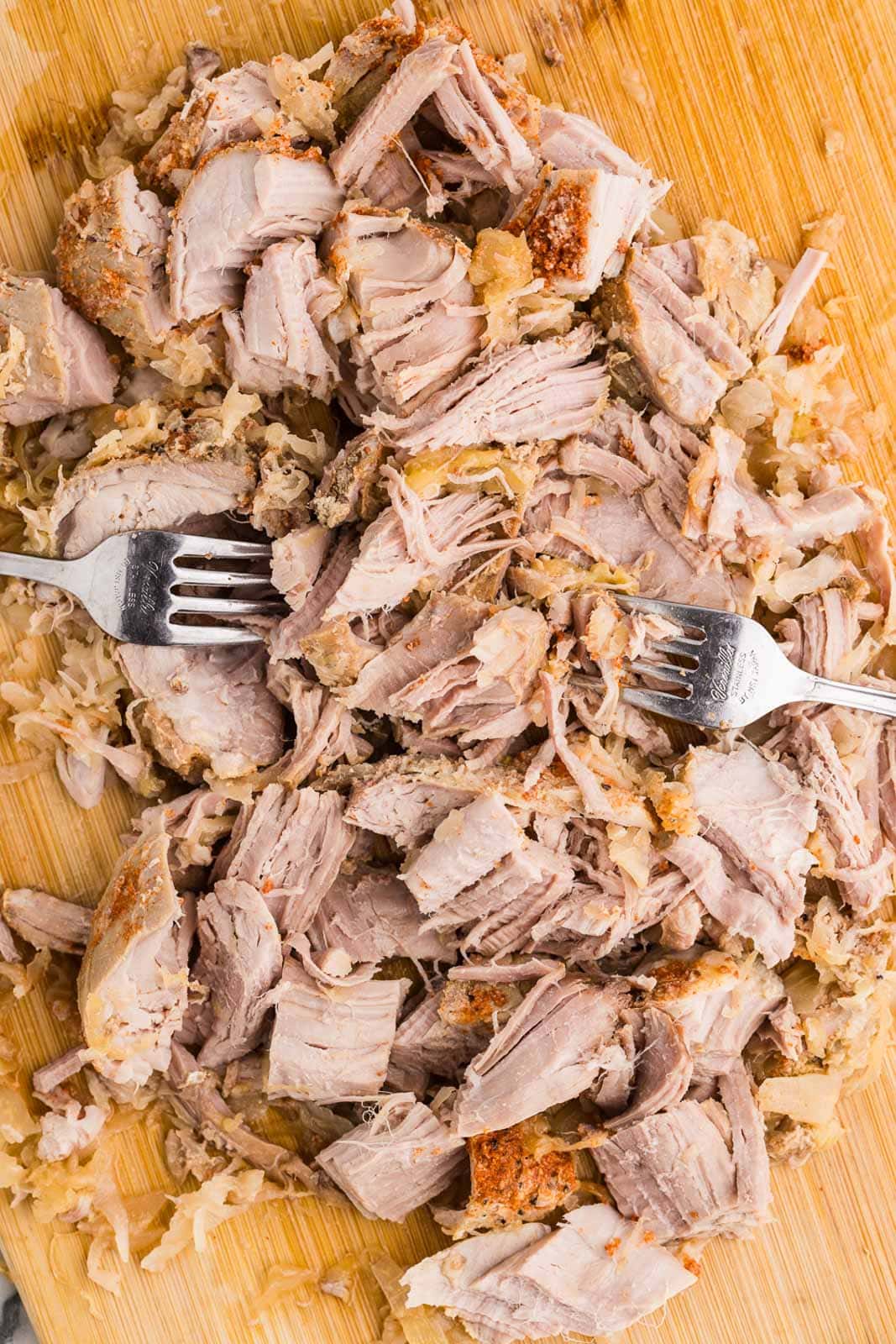 wooden cutting board of shredded pork loin with 2 forks