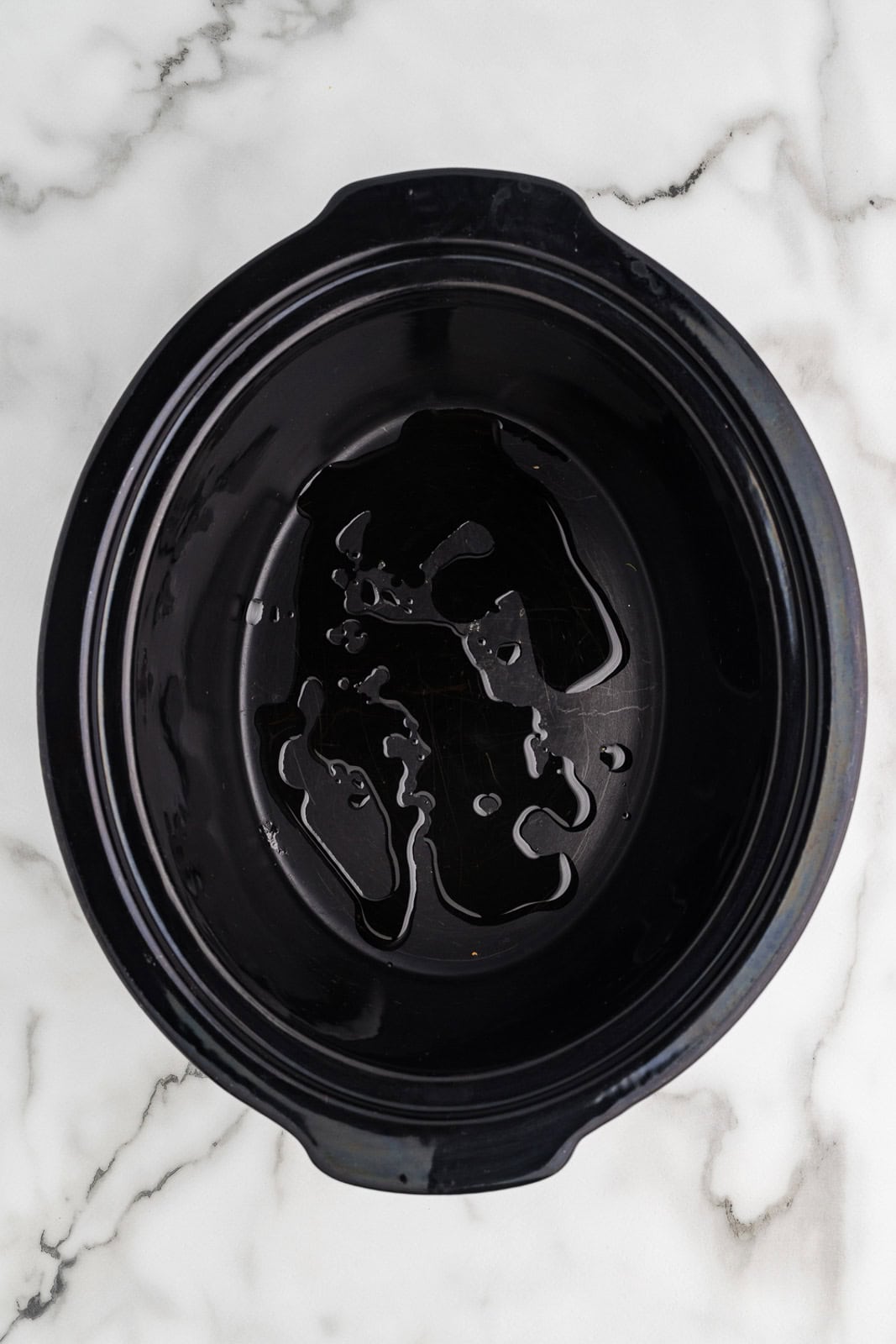 overhead view of black slow cooker with olive oil drizzled on bottom