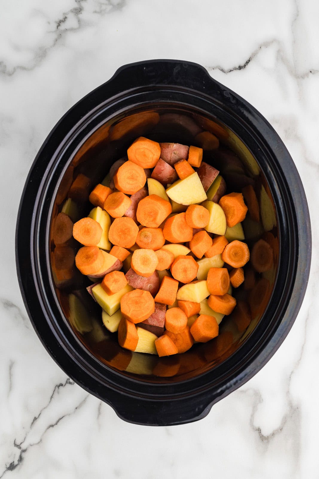 overhead view of black slow cooker with carrots and potatoes