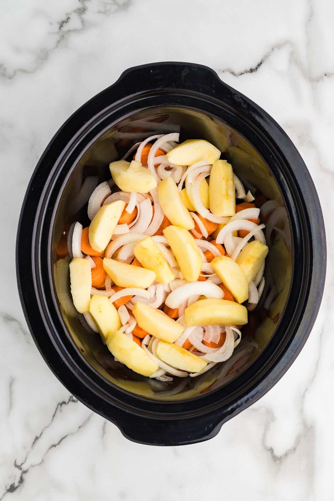 overhead view of black slow cooker with carrots, potatoes, onions and apple slices