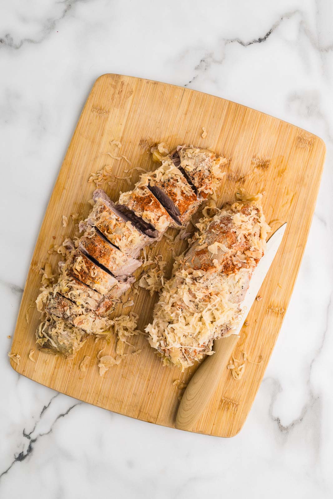 wooden cutting board with 2 pieces of slow cooked pork loin, half sliced, with knife on side