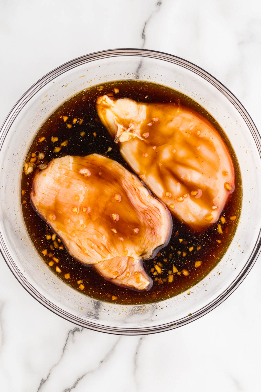 overhead view of glass bowl with marinade and 2 chicken breasts