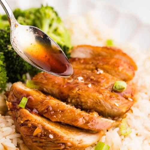 closeup of cooked marinated chicken on a bed of rice with broccoli on side with spoon holding marinade