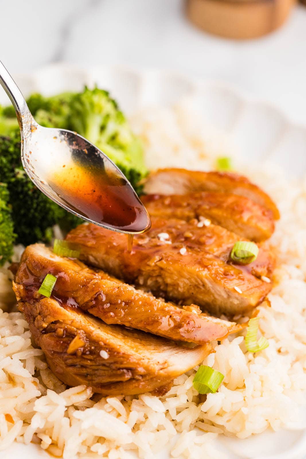 closeup of cooked marinated chicken on a bed of rice with broccoli on side with spoon holding marinade
