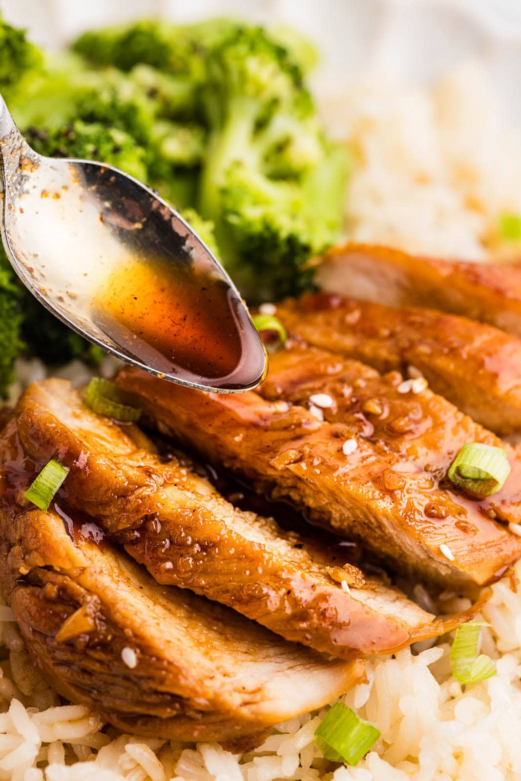 closeup of cooked marinated chicken on a bed of rice with broccoli on side with spoon holding marinade