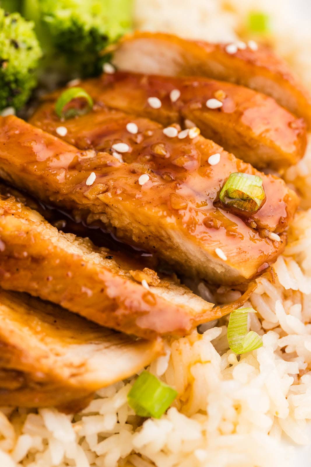 closeup of cooked marinated chicken on a bed of rice with broccoli on side with spoon holding marinade