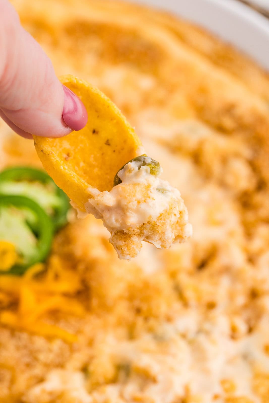 closeup view of hand holding dip on corn chip, with serving bowl of dip in background