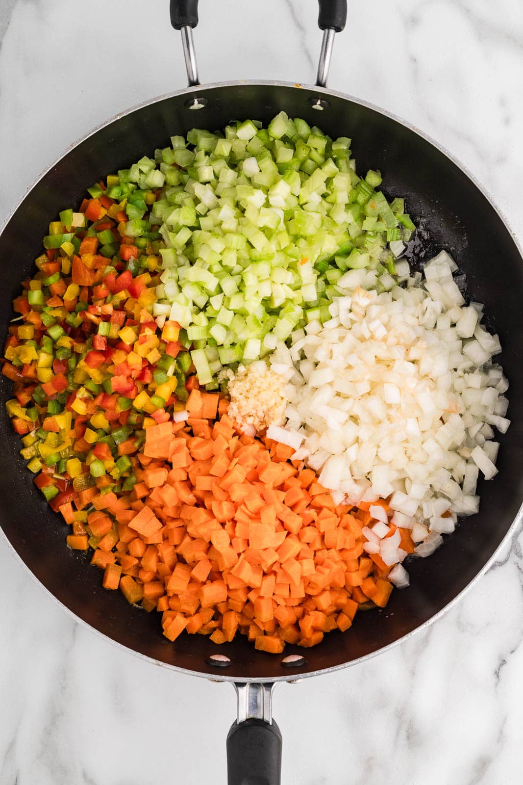 black skillet with diced carrots, peppers, celery and white onion