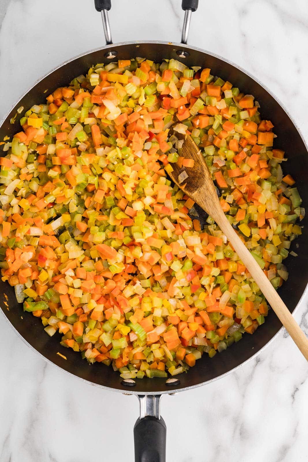 black skillet with sauteed vegetable mixture with wooden spoon