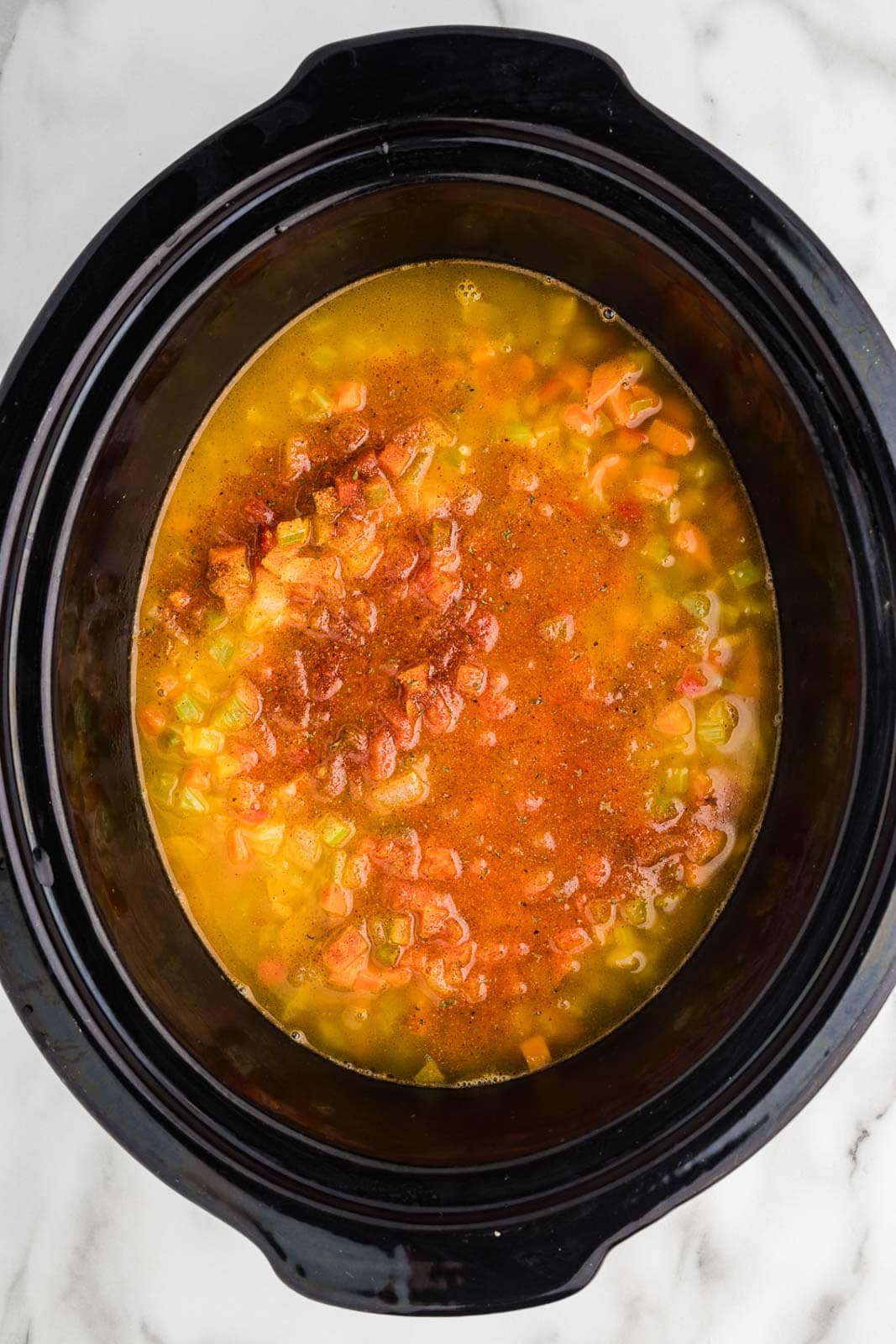 black slow cooker with sausage, vegetable mixture, vegetable broth and seasoning