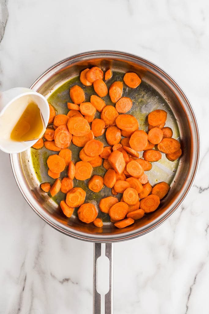 overhead view of cut up carrots in skillet with honey being poured into skillet over carrots