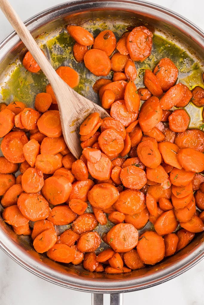 overhead view of skillet with sauteed carrots with wooden spoon