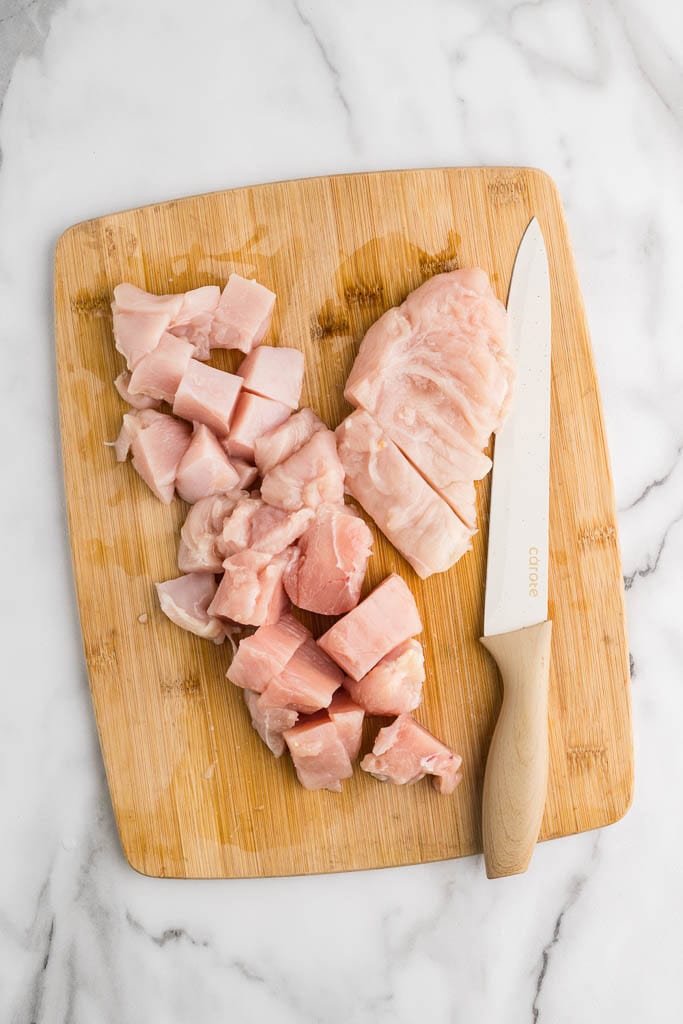 wooden cutting board with chicken breast, some cubed, with knife