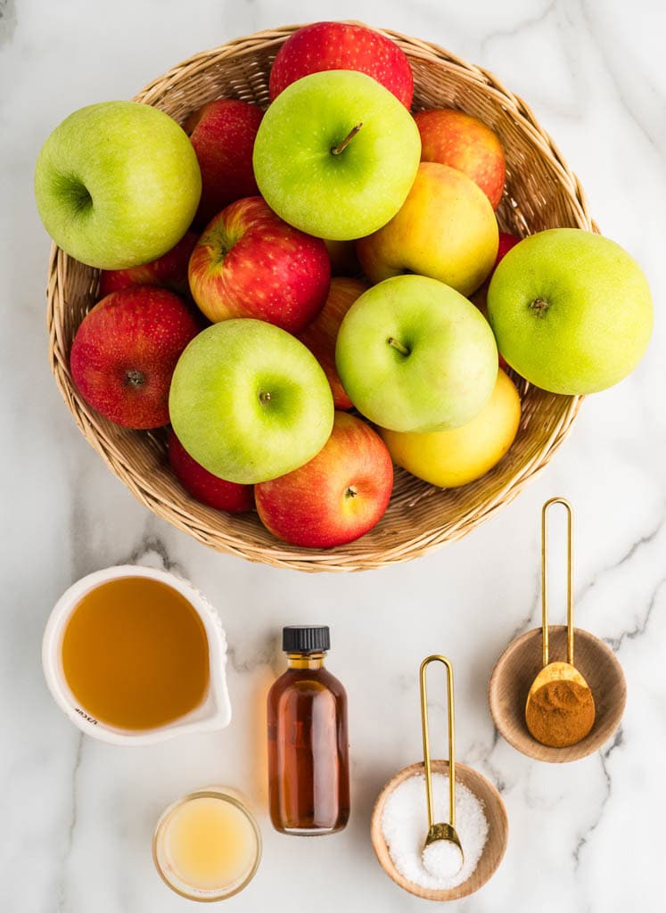 ingredients to include basket of granny Smith and honey crisp apples, surrounded by containers of apple cider vanilla extract, lemon juice, salt and ground cinnamon