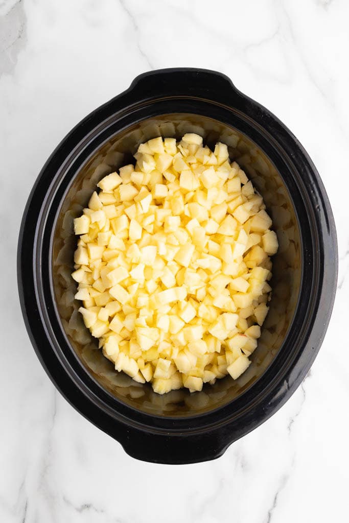 black slow cooker with peeled, cored and chopped apples