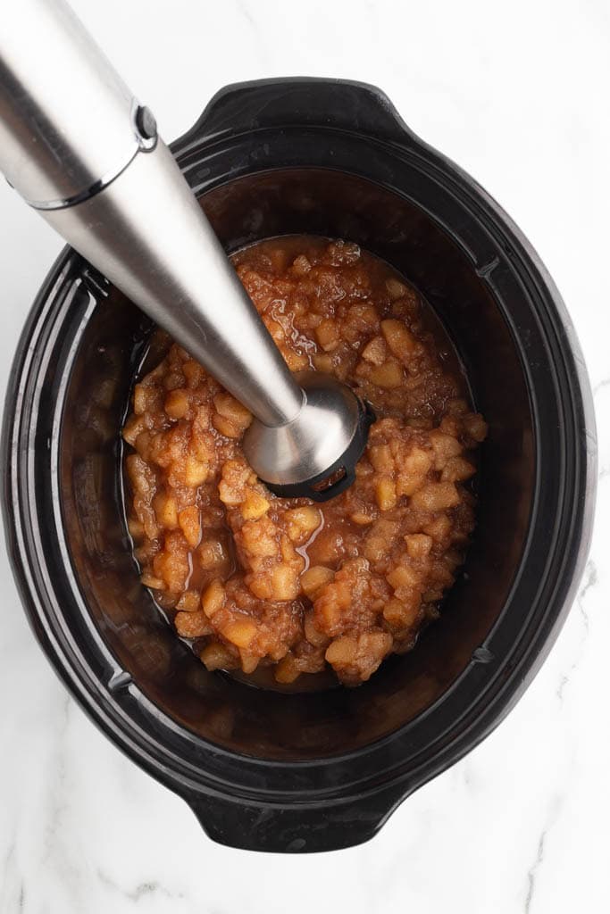 black slow cooker with cooked apples and immersion blender inserted