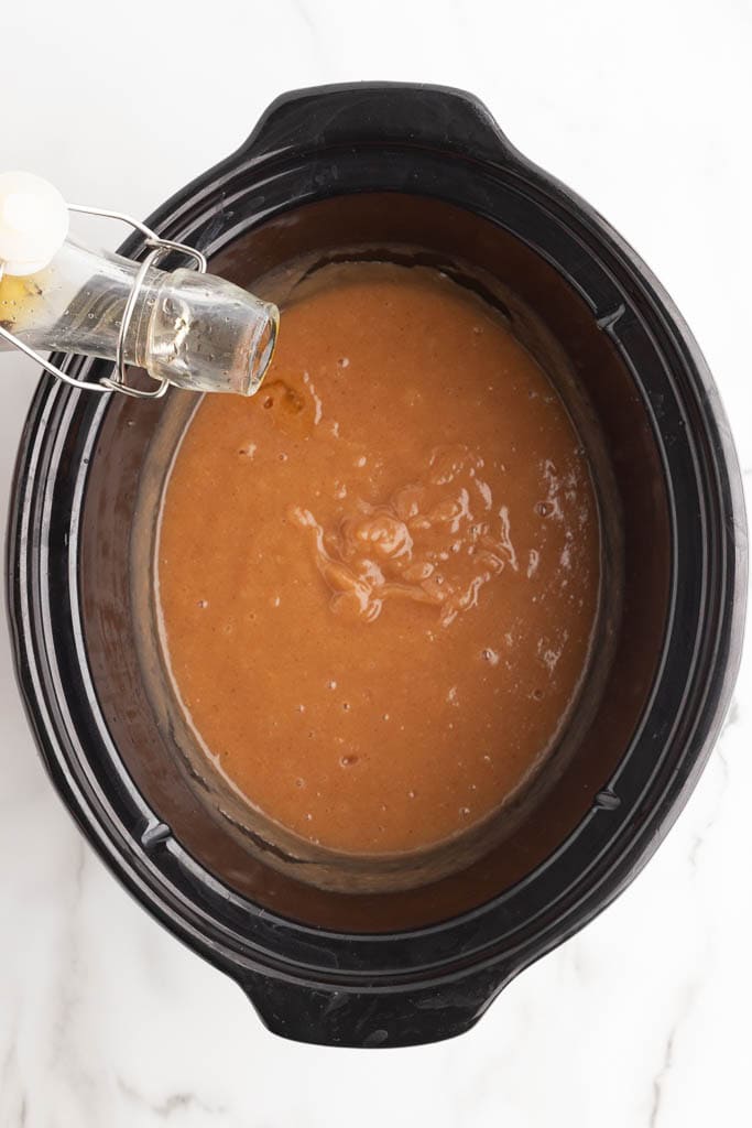 cooked applesauce with container of vanilla extract being poured