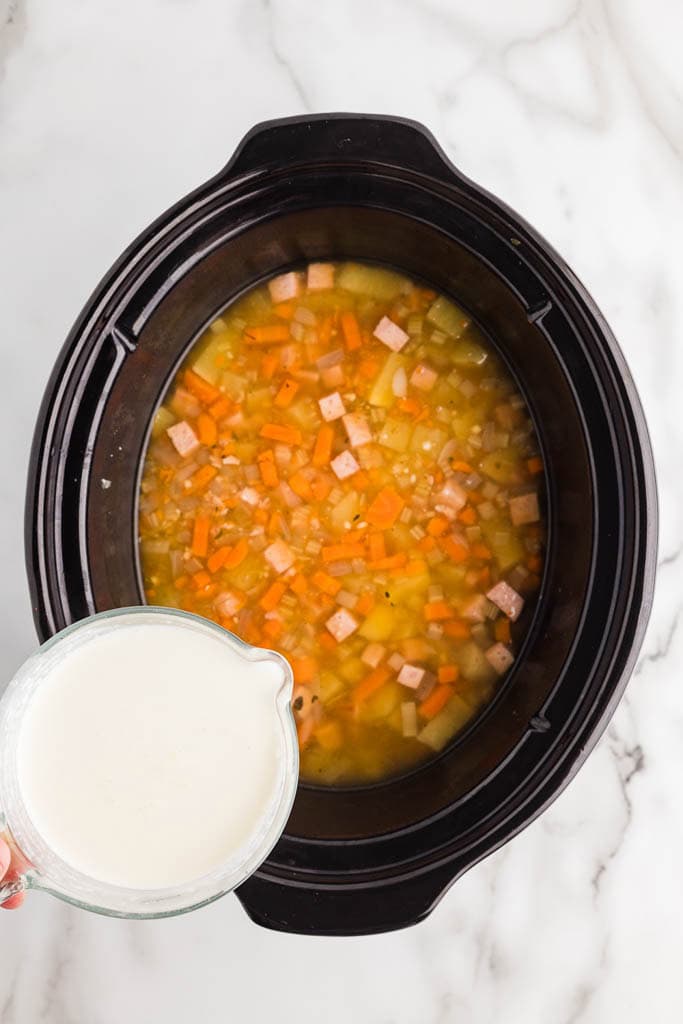 half blended soup mixture with measuring cup of half and half ready to be poured in
