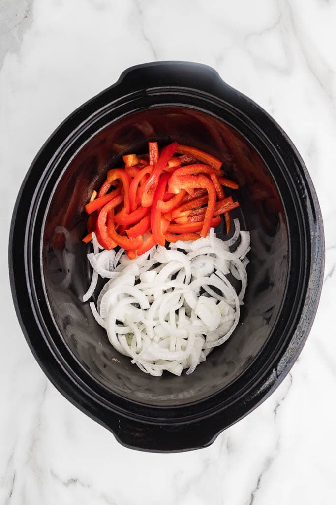 overhead view of black slow cooker onions and red pepper